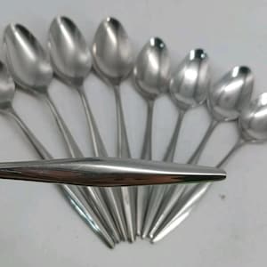 May include: A collection of eight polished stainless steel spoons arranged in a fan pattern. Each spoon features a smooth, tapered handle and a rounded bowl. One spoon is positioned horizontally across the others, highlighting the reflective surface.