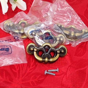 May include: Several antique brass drawer pulls in clear plastic packaging, with the text "MADE IN MEXICO" visible on the packaging. Two screws are also visible. The pulls have a decorative design.