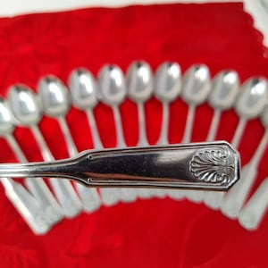 May include: A collection of silver spoons arranged on a red surface. The spoons have a classic design with a decorative element on the handle. The spoons are arranged in a fan shape, with one spoon in focus.