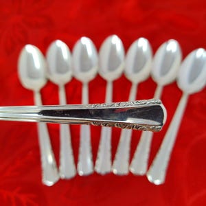 May include: A collection of silver spoons arranged on a red background. The spoons have a classic design with a decorative pattern on the handle. The spoons are reflective, and the image is well-lit, highlighting the details of the silverware.
