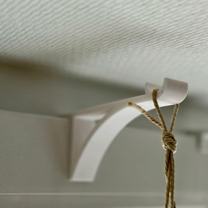 Könnte beinhalten: Ein weißer, an der Decke montierter Halter mit einem braunen Seil, das daran hängt.