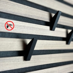 Könnte beinhalten: Eine Holz-Wandverkleidung mit schwarzen Streifen und einem roten Kreis mit einem durchgestrichenen Bohrer-Symbol. An der Wandverkleidung sind drei schwarze Metallhaken angebracht.