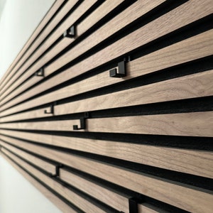 Könnte beinhalten: Ein Wandorganizer mit Holzlatten und schwarzen Metallhaken. Die Latten sind horizontal angeordnet und die Haken sind an den Latten befestigt.