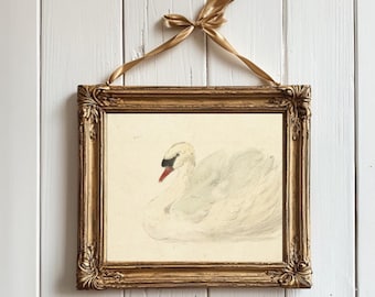 May include: A gold framed picture with a white swan illustration on a white background. The swan is facing left and has a red beak and black eyes.