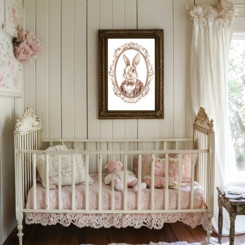 May include: A white crib with a pink and white blanket and a stuffed animal. A framed print of a rabbit in a suit hangs on the wall behind the crib.