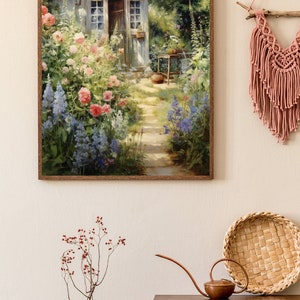 May include: A framed painting of a small cottage with a garden in front of it. The cottage is painted in shades of gray and white, with a brown roof. The garden is filled with colorful flowers, including pink, red, and blue blooms. The painting is set against a background of green trees and a blue sky.