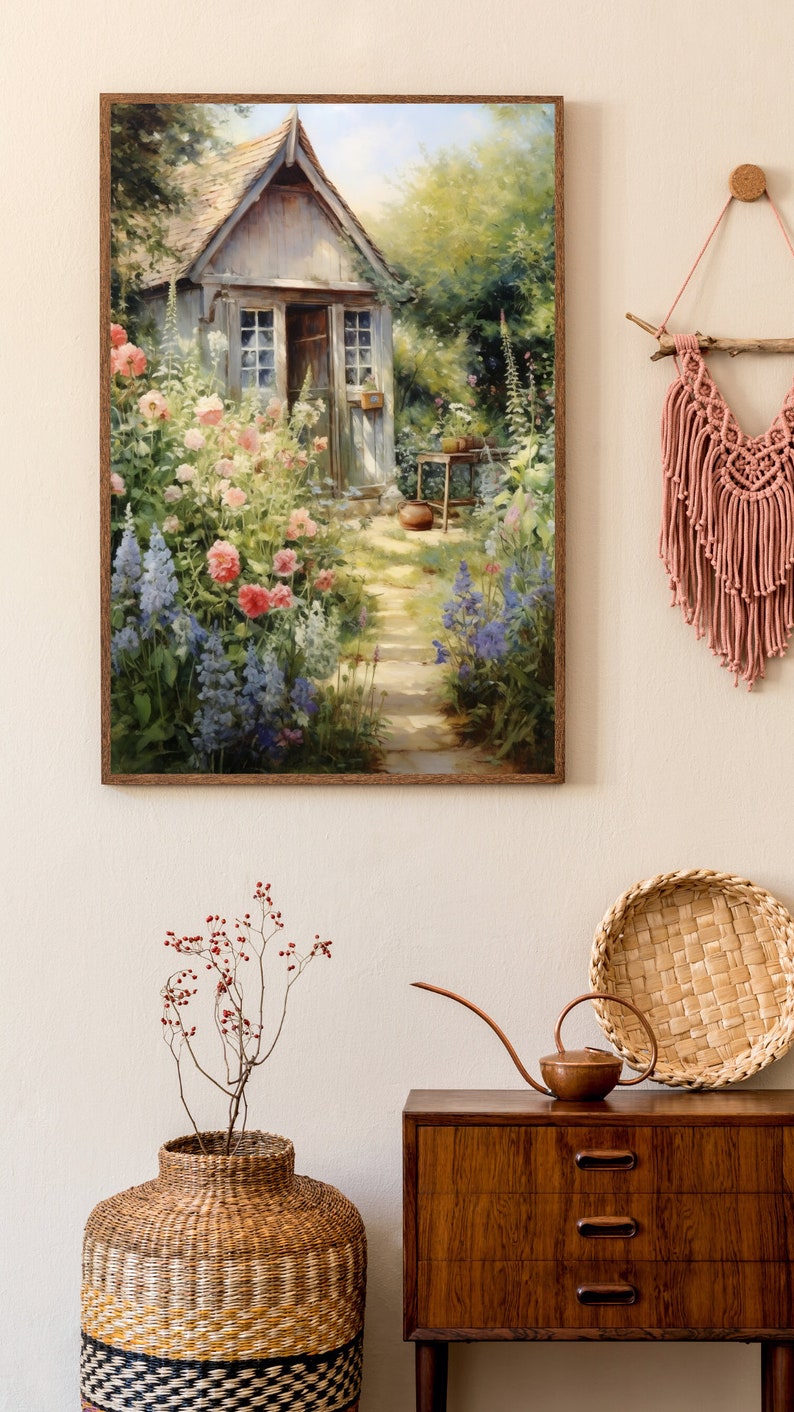 May include: A framed painting of a small cottage with a garden in front of it. The cottage is painted in shades of gray and white, with a brown roof. The garden is filled with colorful flowers, including pink, red, and blue blooms. The painting is set against a background of green trees and a blue sky.