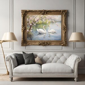 May include: A framed painting of two white swans swimming in a lake with a blooming tree in the background. The painting is in a gold frame with ornate details.