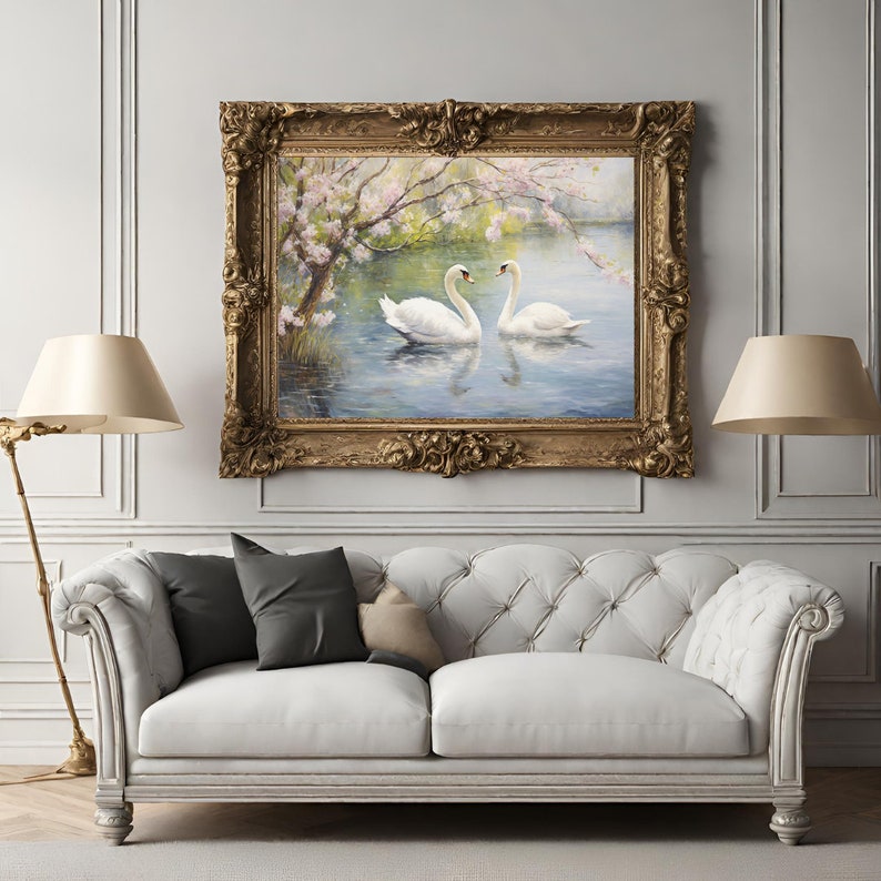 May include: A framed painting of two white swans swimming in a lake with a blooming tree in the background. The painting is in a gold frame with ornate details.