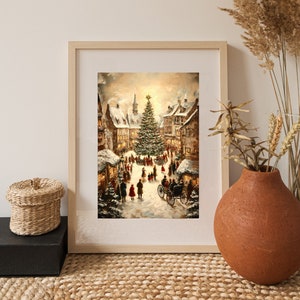 May include: A framed print of a winter scene depicting a Christmas market in a European town square. The artwork features a large Christmas tree, snow-covered buildings, and figures in period clothing. The frame is light-colored wood.