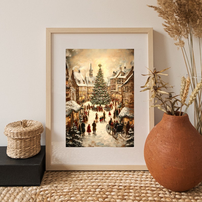 May include: A framed print of a winter scene depicting a Christmas market in a European town square. The artwork features a large Christmas tree, snow-covered buildings, and figures in period clothing. The frame is light-colored wood.