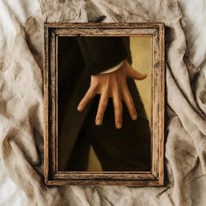 May include: A rectangular wooden frame containing a painting of a hand resting against a dark suit jacket. The hand is positioned centrally, with fingers splayed against the fabric. The background of the painting is a muted, warm yellow tone.