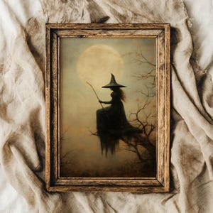 May include: A framed print depicting a witch in a black dress and hat, seated on a tree branch, holding a wand, with a full moon in the background. The artwork has a vintage, gothic aesthetic with muted colours and a rustic wooden frame.