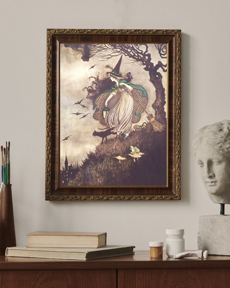 May include: A framed vintage illustration of a witch flying on a broomstick with a black cat and bats in the background. The witch is wearing a green dress and a pointed hat. The illustration is set against a dark, stormy sky.
