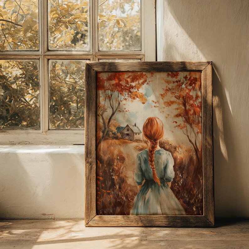 May include: A framed art print featuring a painting of a person with red hair in a blue dress, walking away on a path towards a small house. The artwork is set in an autumn landscape with trees and foliage in shades of orange and brown.