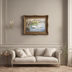 May include: A framed painting of two white swans swimming in a lake with a blooming tree in the background. The frame is ornate and gold.