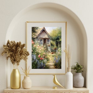 May include: A framed painting of a small cottage with a garden in front. The cottage is painted in shades of gray and white, with a wooden door and windows. The garden is filled with pink and blue flowers, and a path leads to the cottage.