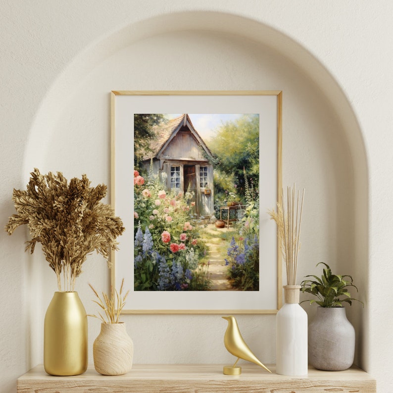 May include: A framed painting of a small cottage with a garden in front. The cottage is painted in shades of gray and white, with a wooden door and windows. The garden is filled with pink and blue flowers, and a path leads to the cottage.