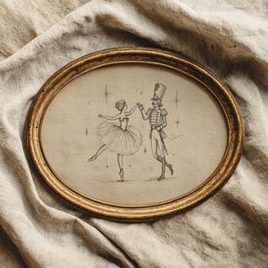 Peut inclure: Un cadre ovale de couleur or vieilli contenant un dessin au trait sur fond beige. L'illustration représente une ballerine en tutu dansant avec un soldat casse-noisette, entourés de petites étincelles en forme d'étoile dans l'air.