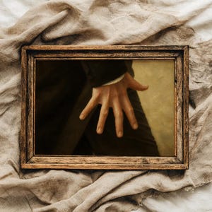 May include: A rectangular wooden picture frame with a dark brown finish containing a print of a hand with fingers spread wide against a dark garment. The frame has a visible wood grain texture and is constructed with mitered corners.