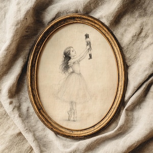 May include: An oval-shaped gold frame containing a pencil sketch of a young dancer in a tutu standing on pointe shoes. The dancer holds a small nutcracker figure high above their head with both hands. The artwork is rendered in soft graphite tones.