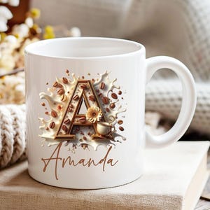 Może przedstawiać: Biały ceramiczny kubek z motywem kawowym. Projekt przedstawia literę "A" w kolorze brązowym, ziarna kawy, małą filiżankę i imię "Amanda" w ozdobnej czcionce.