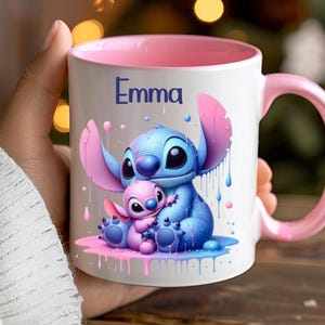 K&ouml;nnte beinhalten: Eine wei&szlig;e Keramiktasse mit rosafarbenem Rand und Henkel. Die Tasse zeigt eine farbenfrohe Illustration von Stitch und Angel aus dem Disney-Film Lilo & Stitch. Die Tasse ist mit dem Namen "Emma" personalisiert.