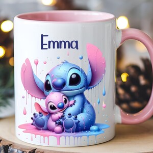 K&ouml;nnte beinhalten: Eine wei&szlig;e Keramiktasse mit rosafarbenem Rand und Henkel. Die Tasse zeigt eine farbenfrohe Illustration von Stitch und Angel aus dem Disney-Film Lilo & Stitch. Der Text "Emma" ist auf die Tasse gedruckt.