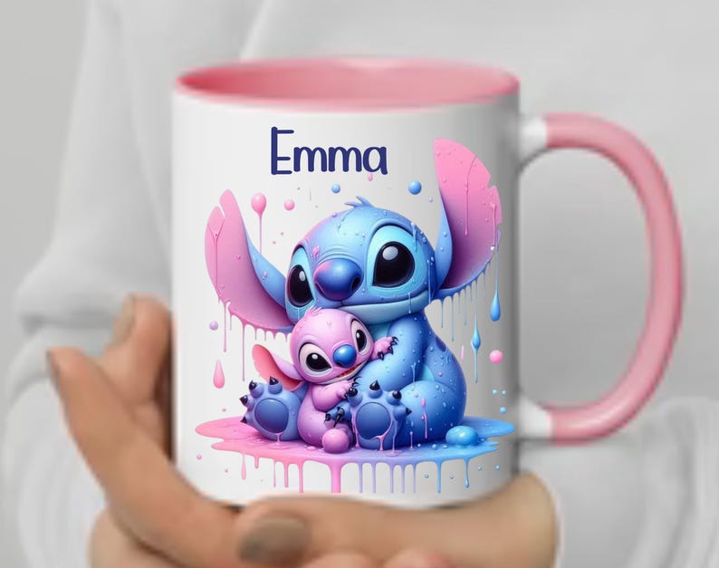 K&ouml;nnte beinhalten: Eine wei&szlig;e Keramiktasse mit rosafarbenem Rand und Henkel. Die Tasse zeigt eine farbenfrohe Illustration von Stitch und Angel aus dem Disney-Film Lilo & Stitch. Der Text "Emma" ist auf die Tasse gedruckt.