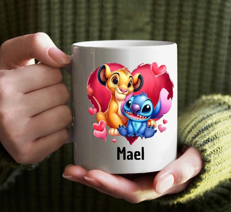 Puede incluir: Taza de cer&aacute;mica blanca con una ilustraci&oacute;n colorida de Simba de El Rey Le&oacute;n y Stitch de Lilo & Stitch dentro de un coraz&oacute;n rojo. El texto "Mael" est&aacute; impreso debajo de la imagen.