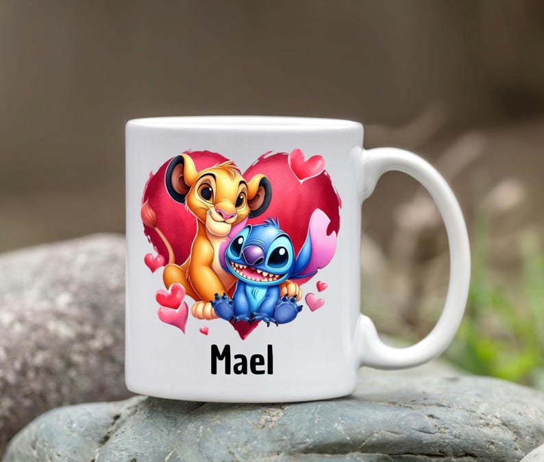 Puede incluir: Taza de cer&aacute;mica blanca con un dise&ntilde;o de coraz&oacute;n rojo que presenta un le&oacute;n de dibujos animados y Stitch de Lilo & Stitch. El coraz&oacute;n tiene acentos rosados y el nombre "Mael" est&aacute; impreso debajo del dise&ntilde;o.