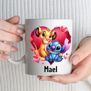 Puede incluir: Taza de cer&aacute;mica blanca con un dise&ntilde;o de coraz&oacute;n rojo que presenta un le&oacute;n de dibujos animados y un personaje azul Stitch. La taza tiene el nombre "Mael" impreso en la parte inferior.