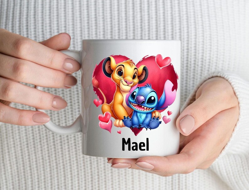 Puede incluir: Taza de cer&aacute;mica blanca con un dise&ntilde;o de coraz&oacute;n rojo que presenta un le&oacute;n de dibujos animados y un personaje azul Stitch. La taza tiene el nombre "Mael" impreso en la parte inferior.