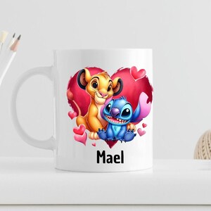 Puede incluir: Taza de cer&aacute;mica blanca con una ilustraci&oacute;n colorida de Simba de El Rey Le&oacute;n y Stitch de Lilo & Stitch. Los personajes est&aacute;n dentro de un coraz&oacute;n rojo con corazones rosas alrededor. La taza tiene el nombre "Mael" impreso en la parte inferior.