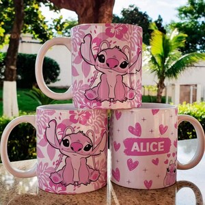 K&ouml;nnte beinhalten: Drei rosa Keramikbecher mit verschiedenen Designs. Ein Becher zeigt eine rosa Stitch-Figur mit einem Blumenmuster. Ein weiterer Becher hat eine rosa Stitch-Figur mit einem Blumenmuster. Der dritte Becher hat ein rosa Herzmuster mit dem Namen "Alice" in Schwarz.