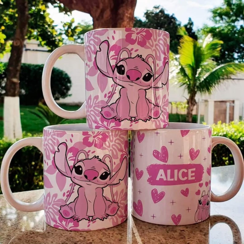 K&ouml;nnte beinhalten: Drei rosa Keramikbecher mit verschiedenen Designs. Ein Becher zeigt eine rosa Stitch-Figur mit einem Blumenmuster. Ein weiterer Becher hat eine rosa Stitch-Figur mit einem Blumenmuster. Der dritte Becher hat ein rosa Herzmuster mit dem Namen "Alice" in Schwarz.