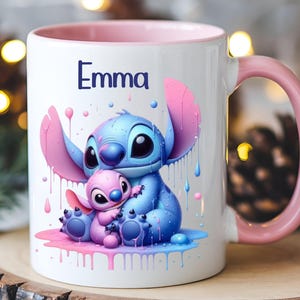 K&ouml;nnte beinhalten: Eine wei&szlig;e Keramiktasse mit rosafarbenem Rand und Henkel. Die Tasse zeigt eine farbenfrohe Illustration von Stitch und Angel aus dem Disney-Film Lilo & Stitch. Der Text "Emma" ist auf die Tasse gedruckt.