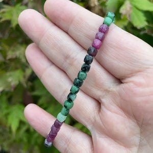 May include: A green, pink and black gemstone bracelet with faceted beads. The bracelet is made of natural stones and is approximately 7 inches in length.