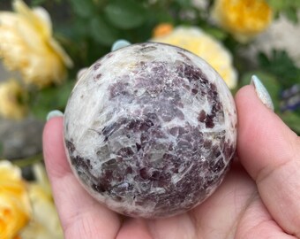 May include: A white and purple Lepidolite sphere crystal ball. The sphere is smooth and polished, with a swirling pattern of purple and white.