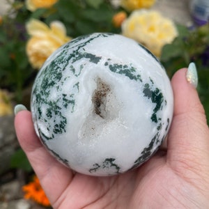 May include: A white and green agate sphere with a natural druzy opening. The sphere is smooth and polished, with a variety of green and white patterns.
