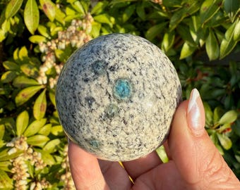 May include: A smooth, white and gray sphere with blue flecks. The sphere is made of polished stone and has a speckled appearance.
