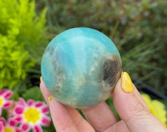 May include: A smooth, polished green and white Amazonite sphere. The sphere has a natural, organic look with swirls and patterns throughout.