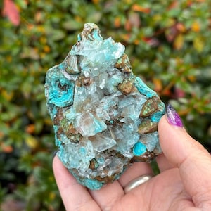 May include: A natural mineral specimen featuring a combination of colors and textures. The piece showcases a mix of crystalline formations in shades of clear and light blue, contrasted with areas of brown and turquoise. The overall shape is irregular and rough.