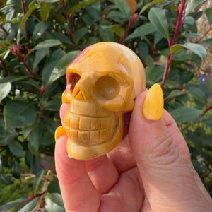 May include: A yellow and red carved skull made of stone. The skull is detailed with a carved mouth and eye sockets.