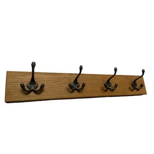 May include: A wooden coat rack with four double hooks. The rack is made of natural wood and has a rustic finish. The hooks are made of metal and have a black finish.