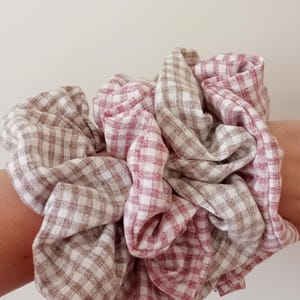 Könnte beinhalten: Ein großer Haargummi aus Stoff mit einem Vichy-Muster in Rosa-, Weiß- und Brauntönen. Der Stoff ist gerafft und zusammengeballt, wodurch ein voluminöses Accessoire entsteht. Das Haargummi ist zum Halten der Haare gedacht.