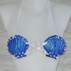 Può includere: Un top all'americana realizzato con due grandi conchiglie di capasanta blu iridescente. Le conchiglie sono decorate con piccole perle bianche e collegate da sottili nastri di raso bianco che si incrociano al centro e formano i laccetti.