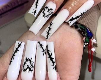 Pode incluir: Unhas acrílicas brancas longas e quadradas com desenhos de arame farpado e coração pretos. As unhas têm um acabamento branco brilhante, com os desenhos pretos adicionando uma estética contrastante e ousada. A nail art é uma declaração ousada.