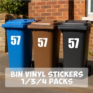 Op de afbeelding: Drie afvalbakken in blauw, bruin en zwart, elk met het nummer 57 in wit. De bakken staan voor een bakstenen muur. De tekst onderaan luidt "BIN VINYL STICKERS 1/3/4 PACKS."