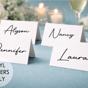 Può includere: Quattro segnaposto bianchi con nomi in elegante scrittura nera: Alyson, Jennifer, Nancy e Laura. I segnaposto sono su una superficie azzurra, con fiori, candele e calici di champagne sullo sfondo. Il testo in basso a sinistra recita "VINYL STICKERS ONLY."